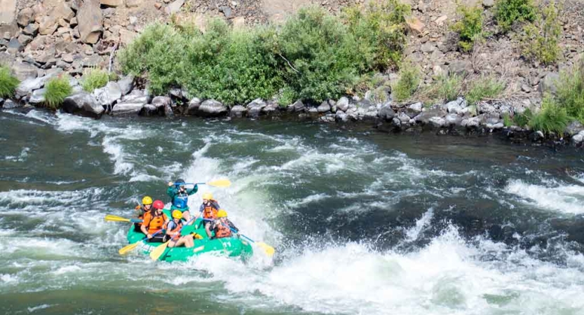 a group of teens navigate whitewater in a raft